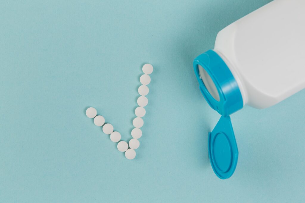 White medication tablets spilling from pill bottle forming a checkmark symbol against blue background.