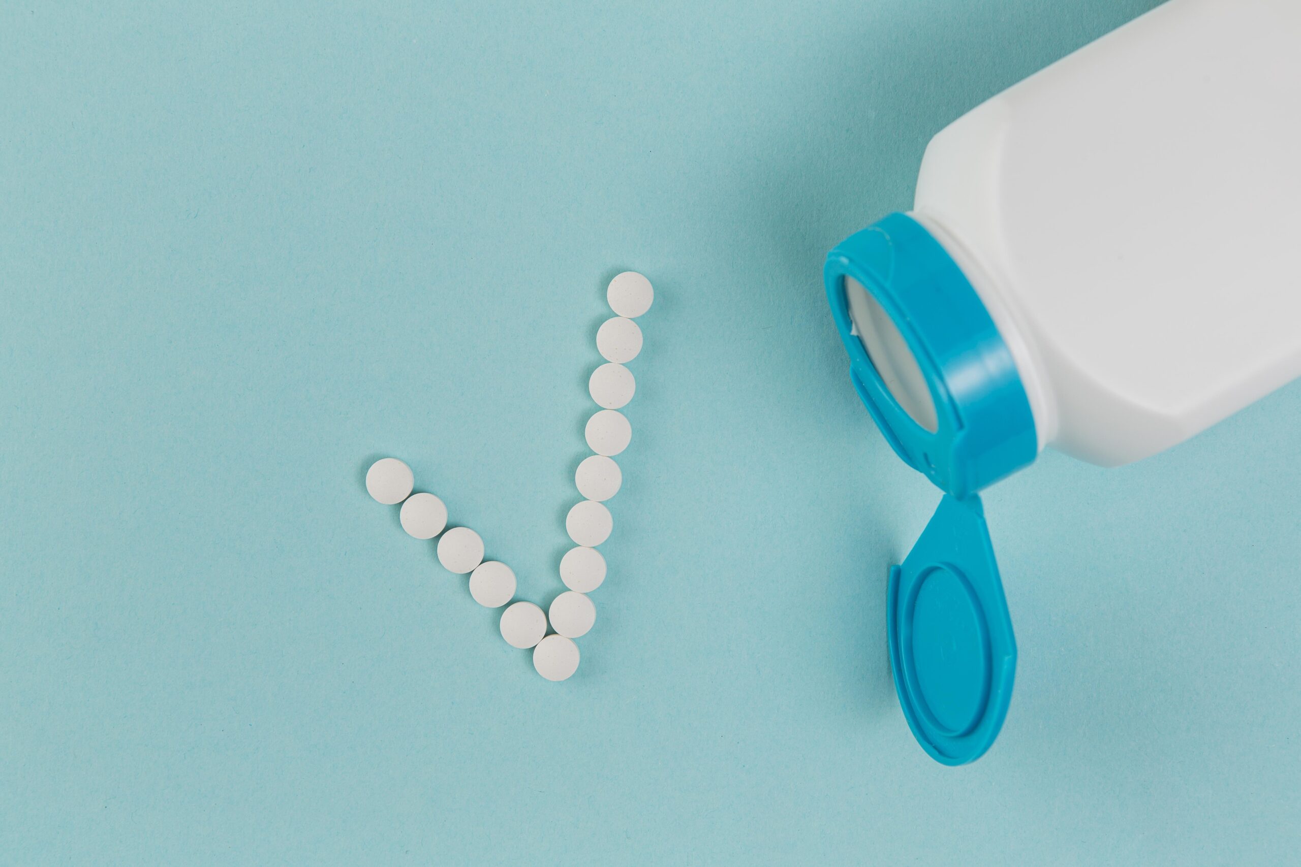 White medication tablets spilling from pill bottle forming a checkmark symbol against blue background.