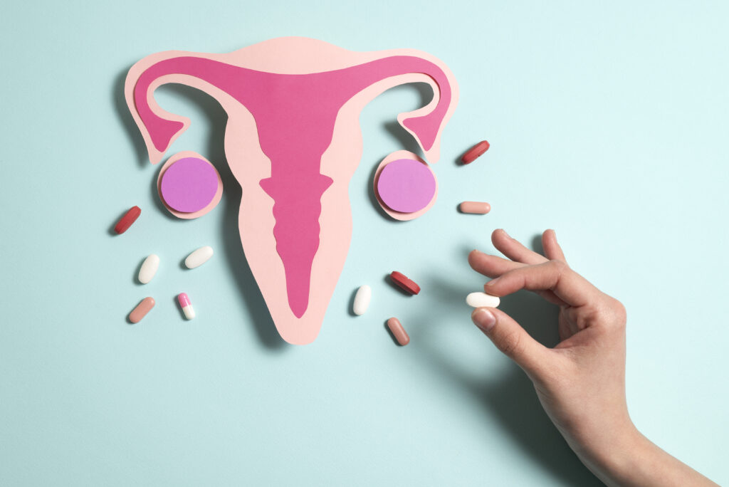 Paper cutout of uterus with surrounding pills and hand holding white pill
