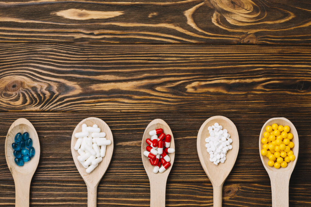 Various pills on wooden spoon laying flat on wood table.
