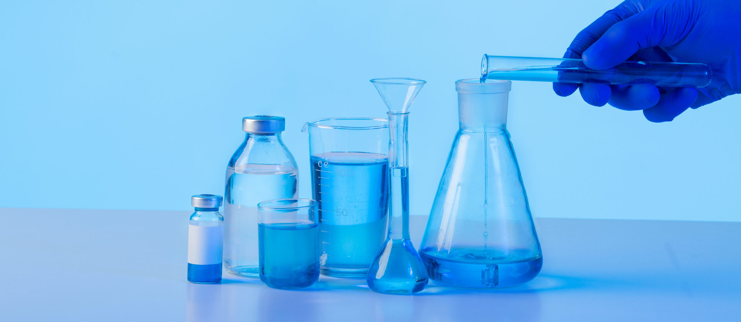 hand in glove pouring blue liquid in lab flask