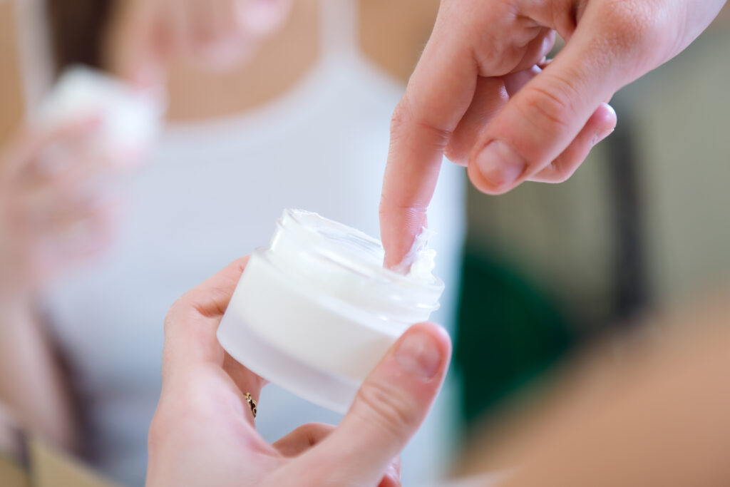 woman dipping finger in container full of medicinal cream