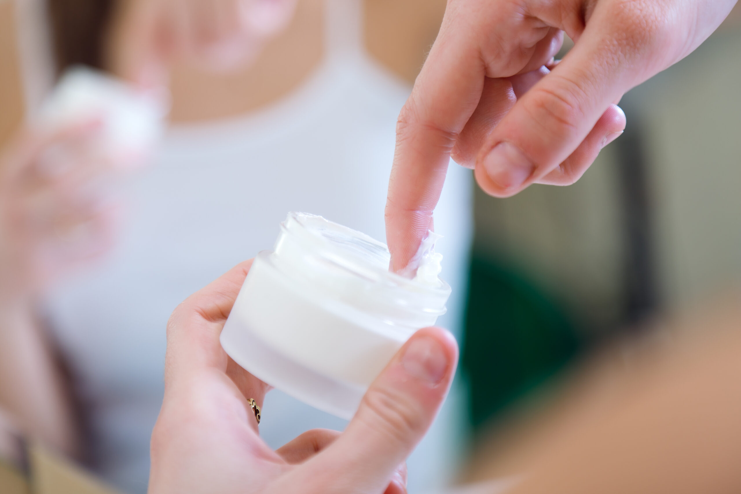 woman dipping finger in container full of medicinal cream