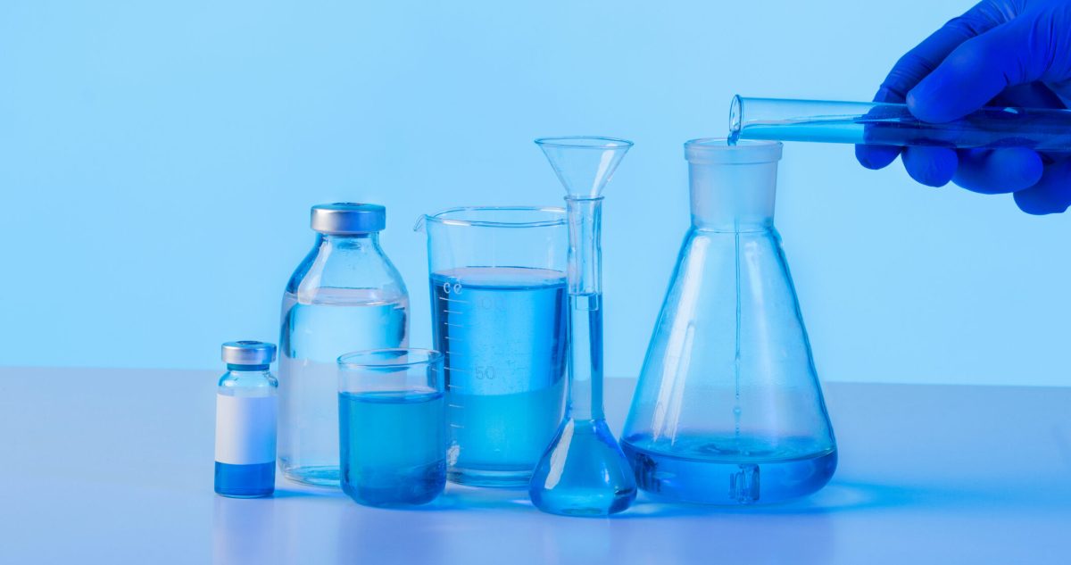 hand in glove pouring blue liquid in lab flask