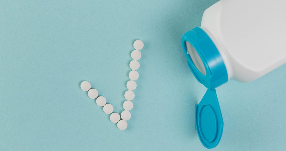 White medication tablets spilling from pill bottle forming a checkmark symbol against blue background.