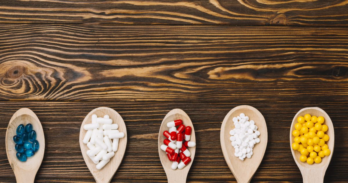 Various pills on wooden spoon laying flat on wood table.
