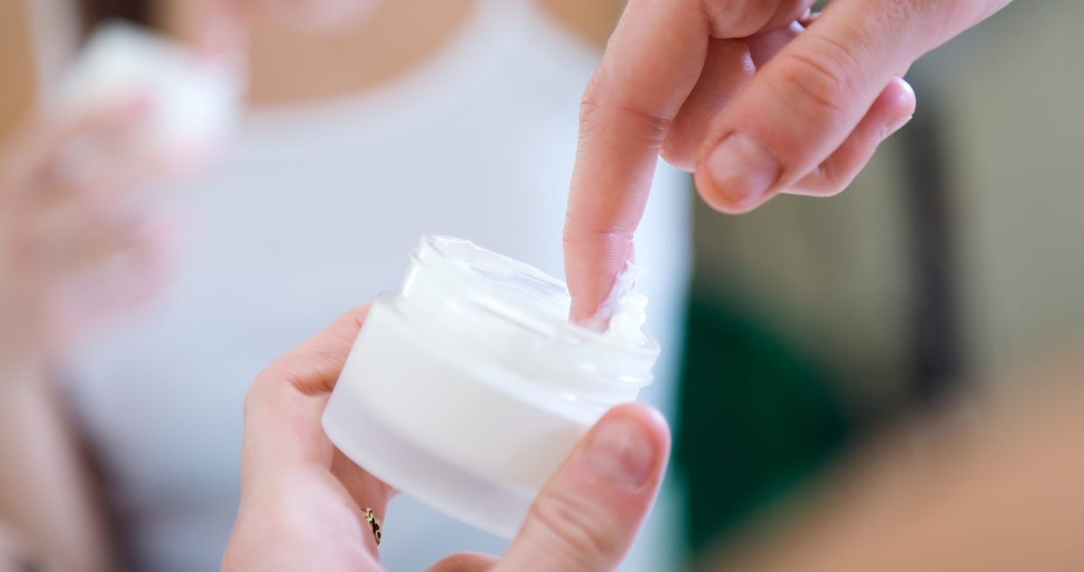 woman dipping finger in container full of medicinal cream